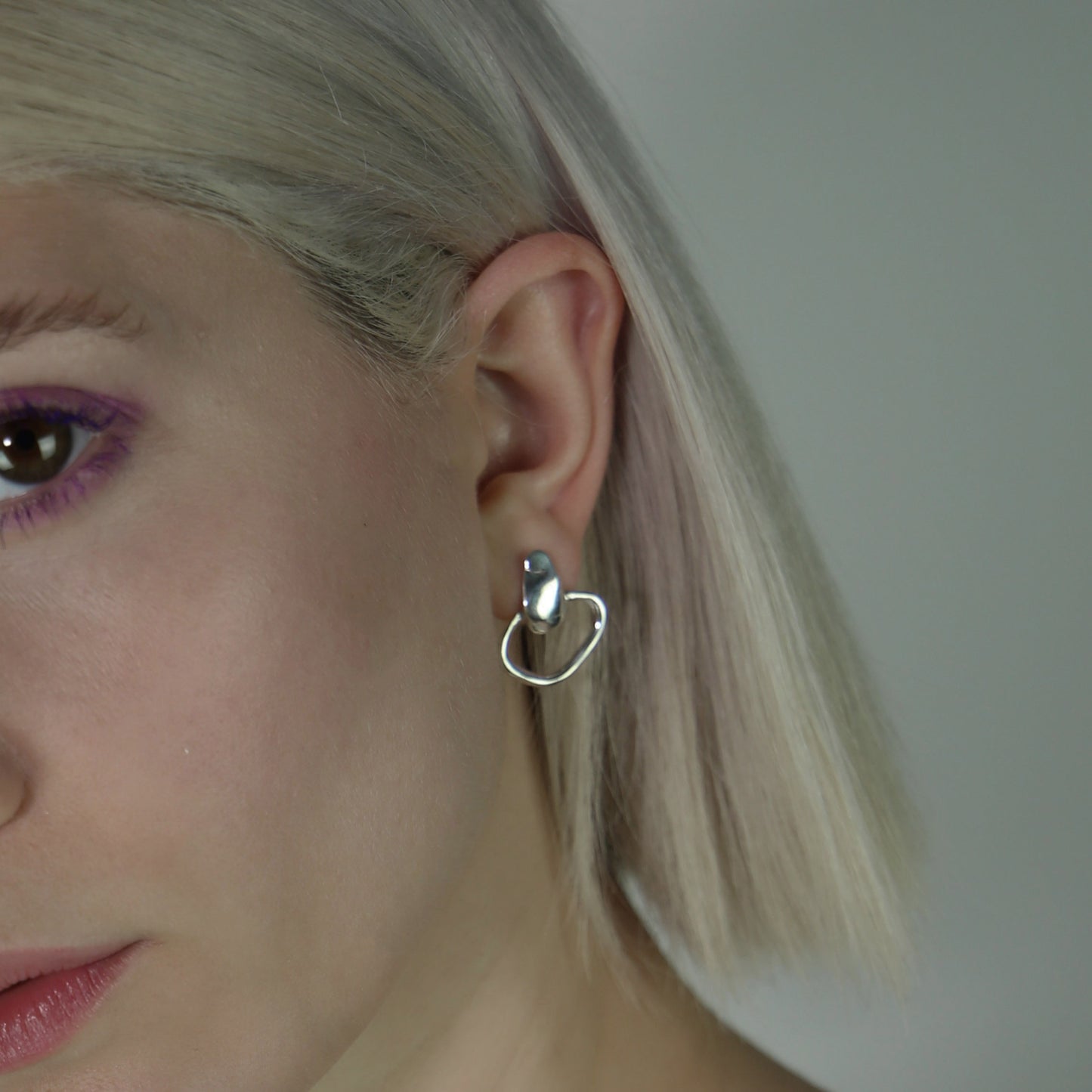 The Circle Drops earrings are a handmade creation crafted from 925 sterling silver. The irregular, smooth, and glossy circle at the bottom creates a unique formation, while the wide silver strip at the top adds a subtle, smooth, and shiny element.