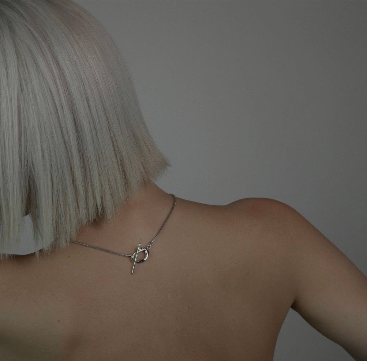 The Kyoto necklace is a handmade piece crafted from 925 sterling silver. Its chain is thick and connected to a small, untreated circle. The fastening is located on the front side