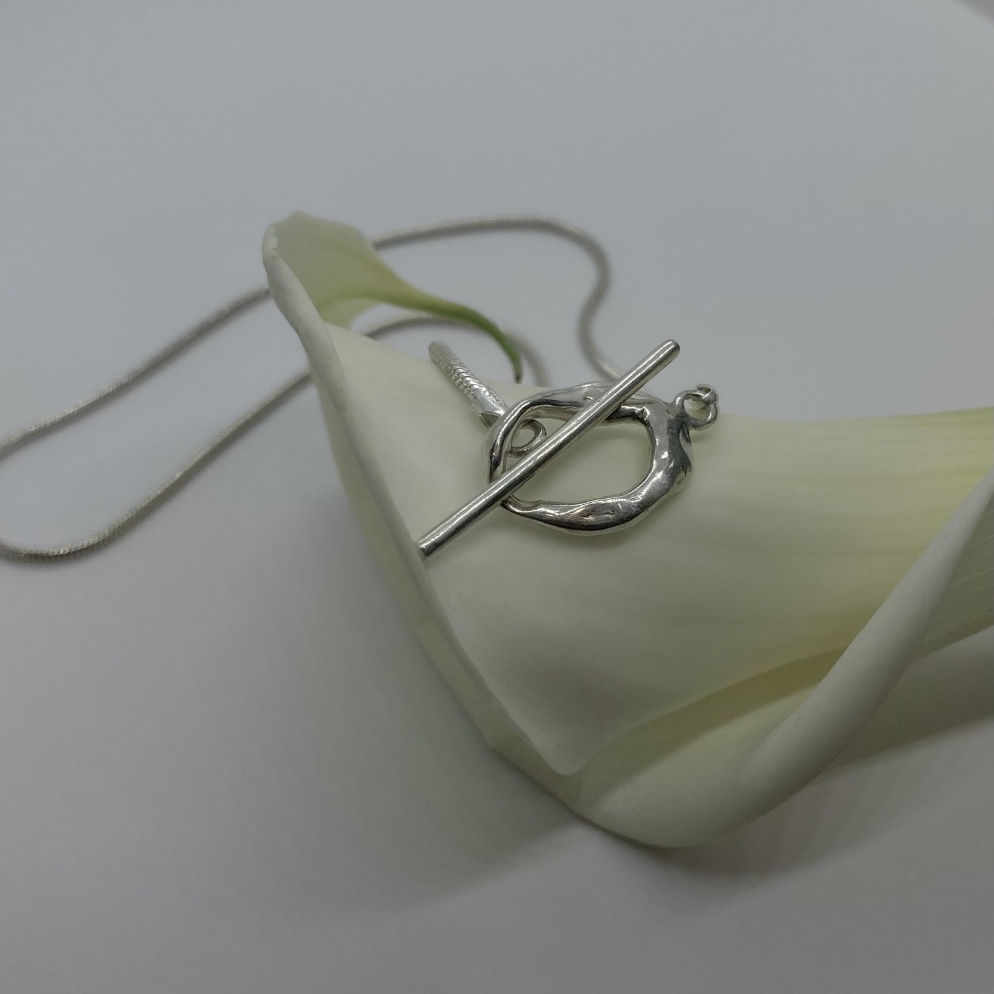 The Kyoto necklace is a handmade piece crafted from 925 sterling silver. Its chain is thick and connected to a small, untreated circle. The fastening is located on the front side