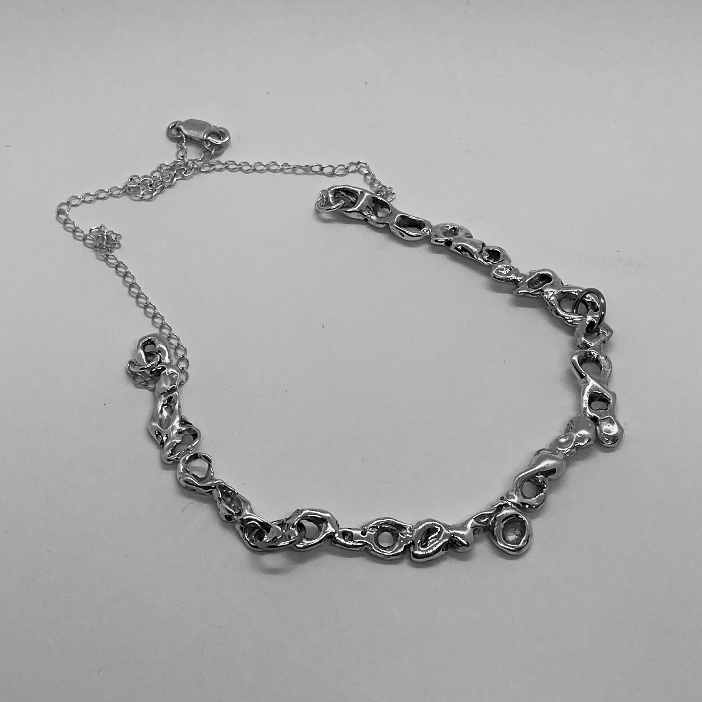 The handmade necklace is made of 925 sterling silver. It features a carved design, and at the end, there is a chain. The surface is polished, giving it a glossy finish