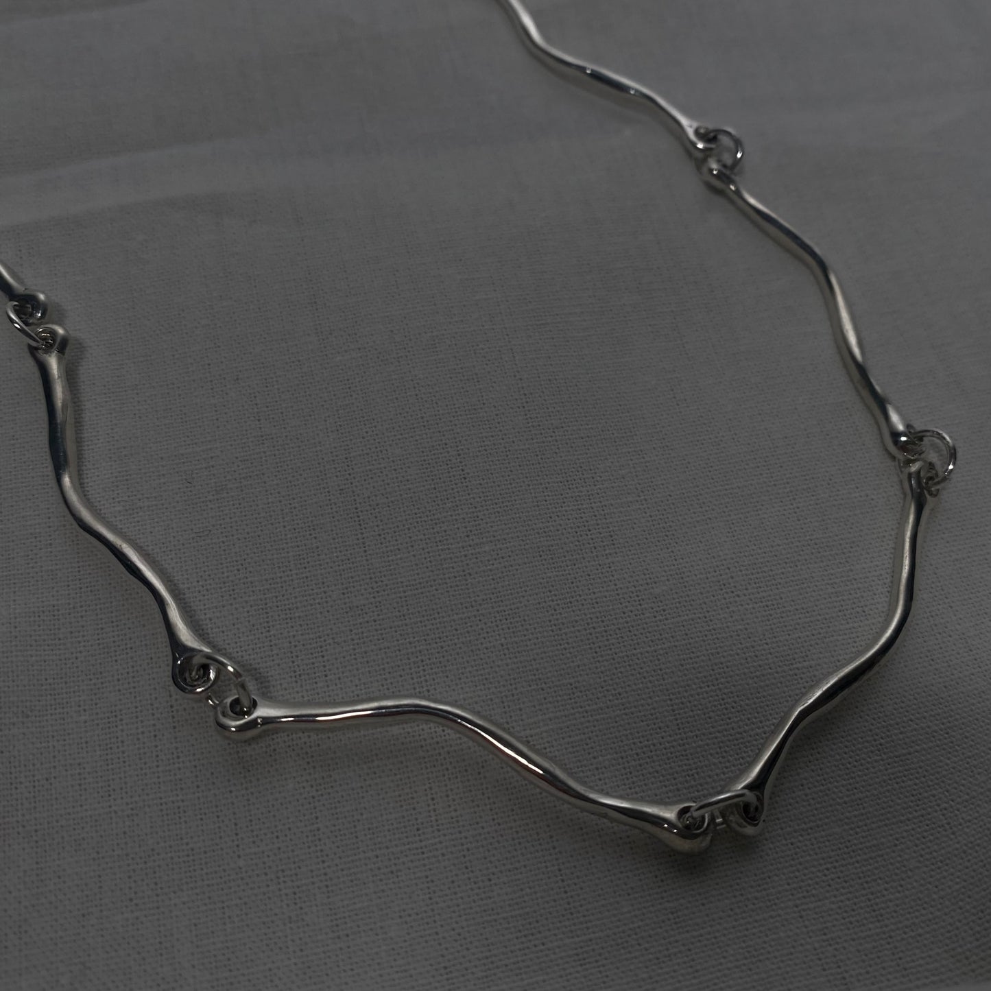The Rogrande necklace is handmade and made of 925 sterling silver. It features small delicate wavy elements connected by rings, creating a smooth and shiny surface