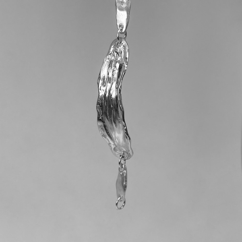 The Amapol bracelet is handmade and crafted from sterling silver 925. It features a raw texture and form, and is polished for a smooth finish. The irregular silver pieces are connected with rings and small oval silver elements.