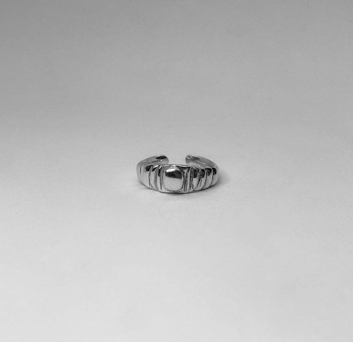 The Arctium ring is a handmade piece made of 925 sterling silver. It features thin lines on its surface and a thick silver circle at its center. It has a glossy finish