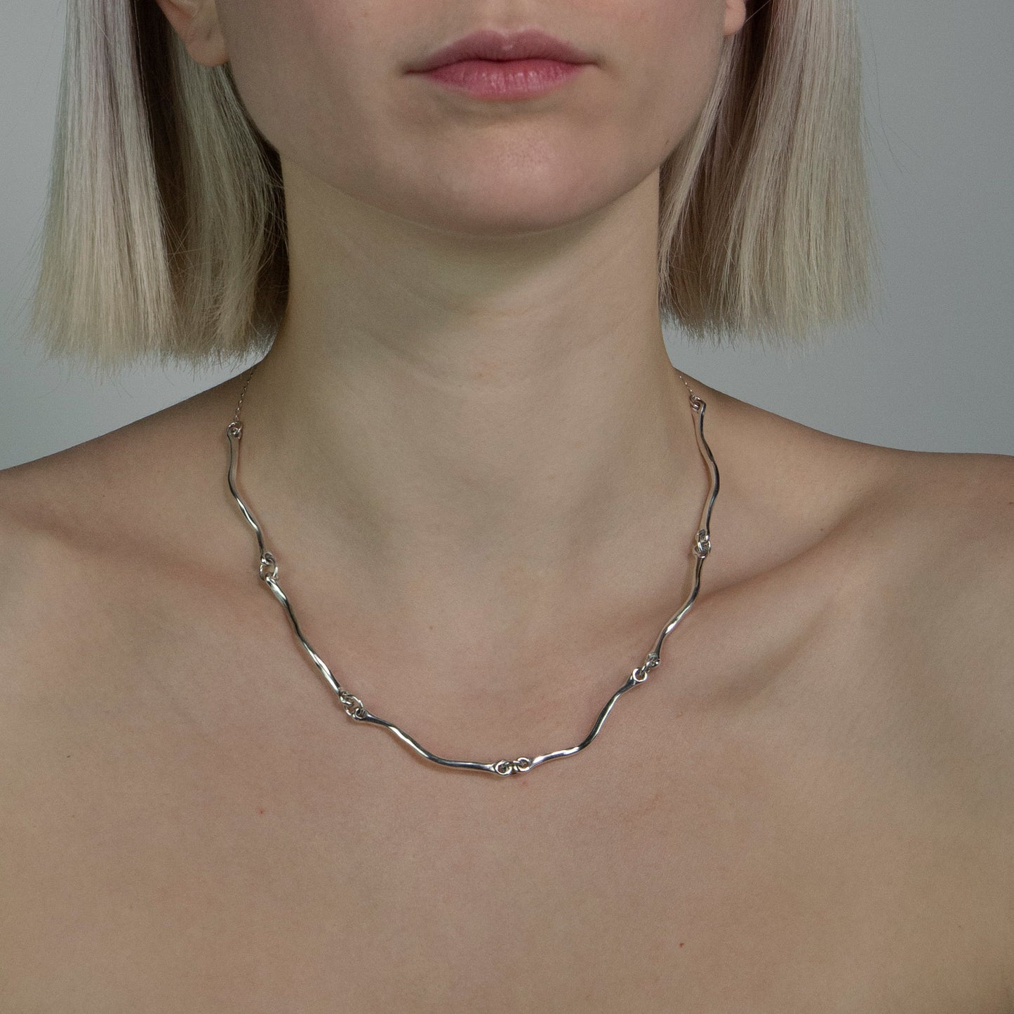 The Rogrande necklace is handmade and made of 925 sterling silver. It features small delicate wavy elements connected by rings, creating a smooth and shiny surface