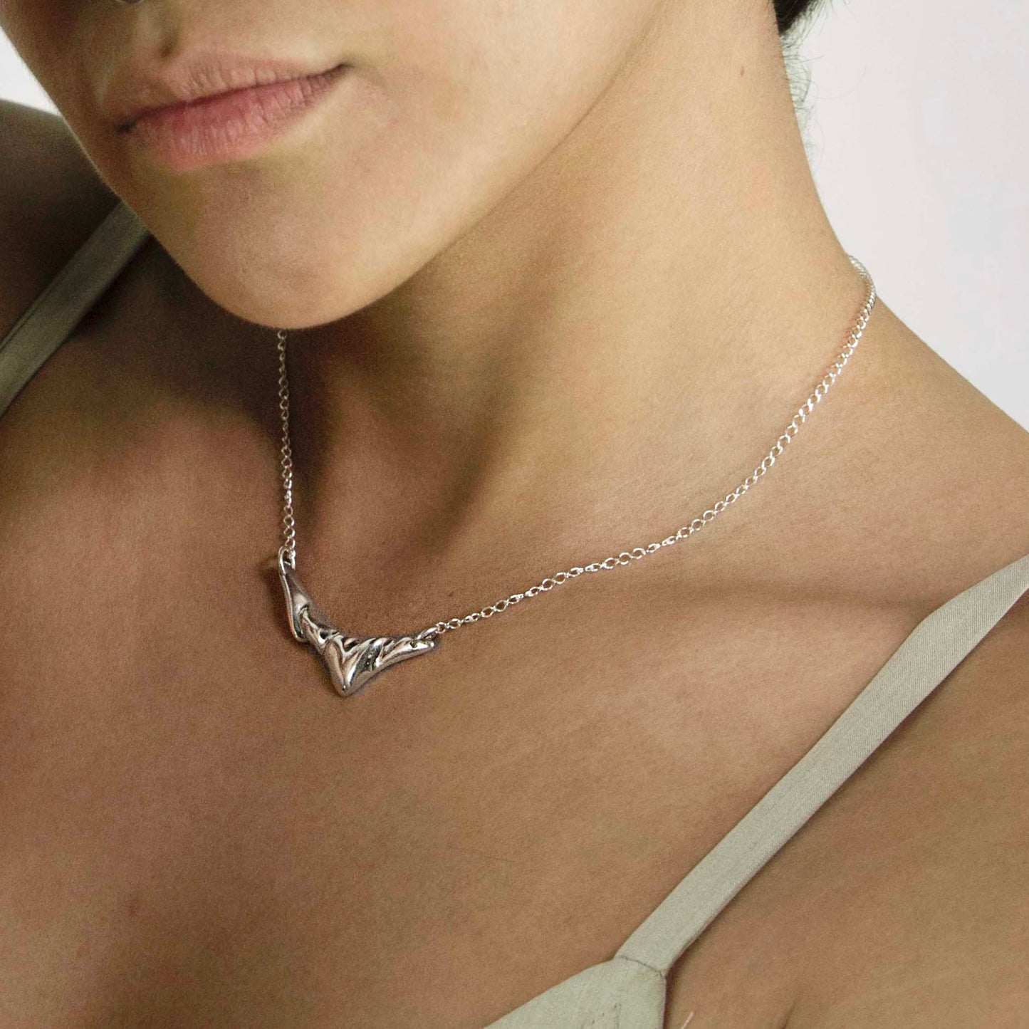 The Regua necklace is a handmade piece made from 925 silver. The necklace features an abstract heart in its center, framed by two irregular wings.