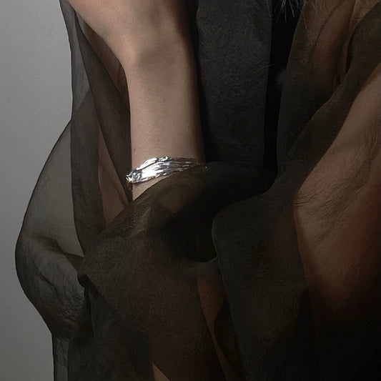 The Amapol bracelet is handmade and crafted from sterling silver 925. It features a raw texture and form, and is polished for a smooth finish. The irregular silver pieces are connected with rings and small oval silver elements.