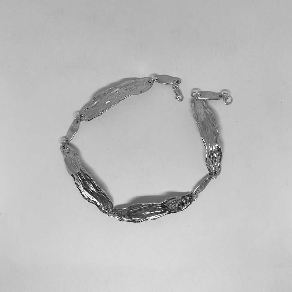 The Lucia necklace is a handmade piece crafted from sterling silver 925. It consists of irregular thin silver plates with a raw texture and form. These plates are connected with rings and small oval silver elements. It is designed to be worn snugly around the neck like a choker and has a polished finish.