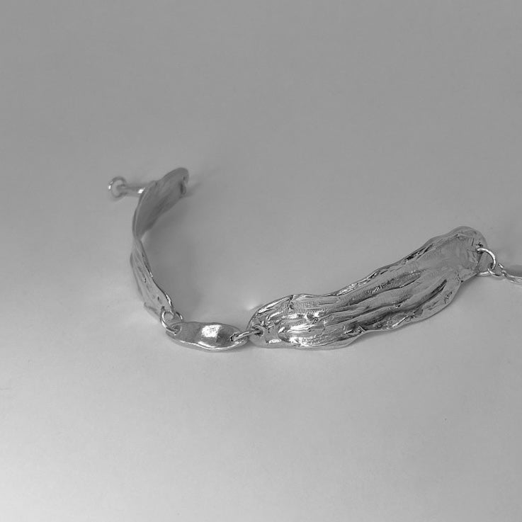 The Amapol bracelet is handmade and crafted from sterling silver 925. It features a raw texture and form, and is polished for a smooth finish. The irregular silver pieces are connected with rings and small oval silver elements.
