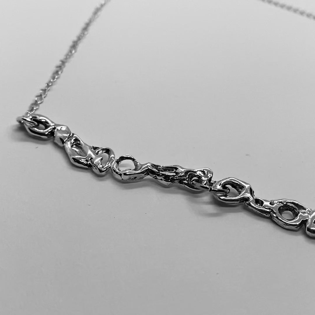  The handmade necklace is made of 925 sterling silver. It features a carved design, and at the end, there is a chain. The surface is polished, giving it a glossy finish